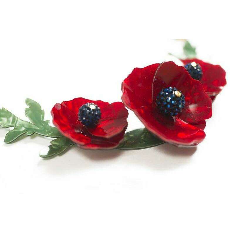 Angled view of red poppy blossoms with blue centers and green leaves on necklace