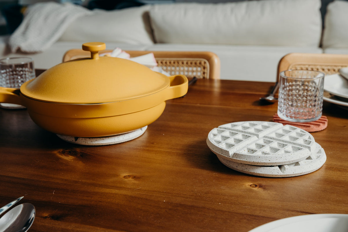 Round white terrazzo waffle trivet on a wooden table near cookware
