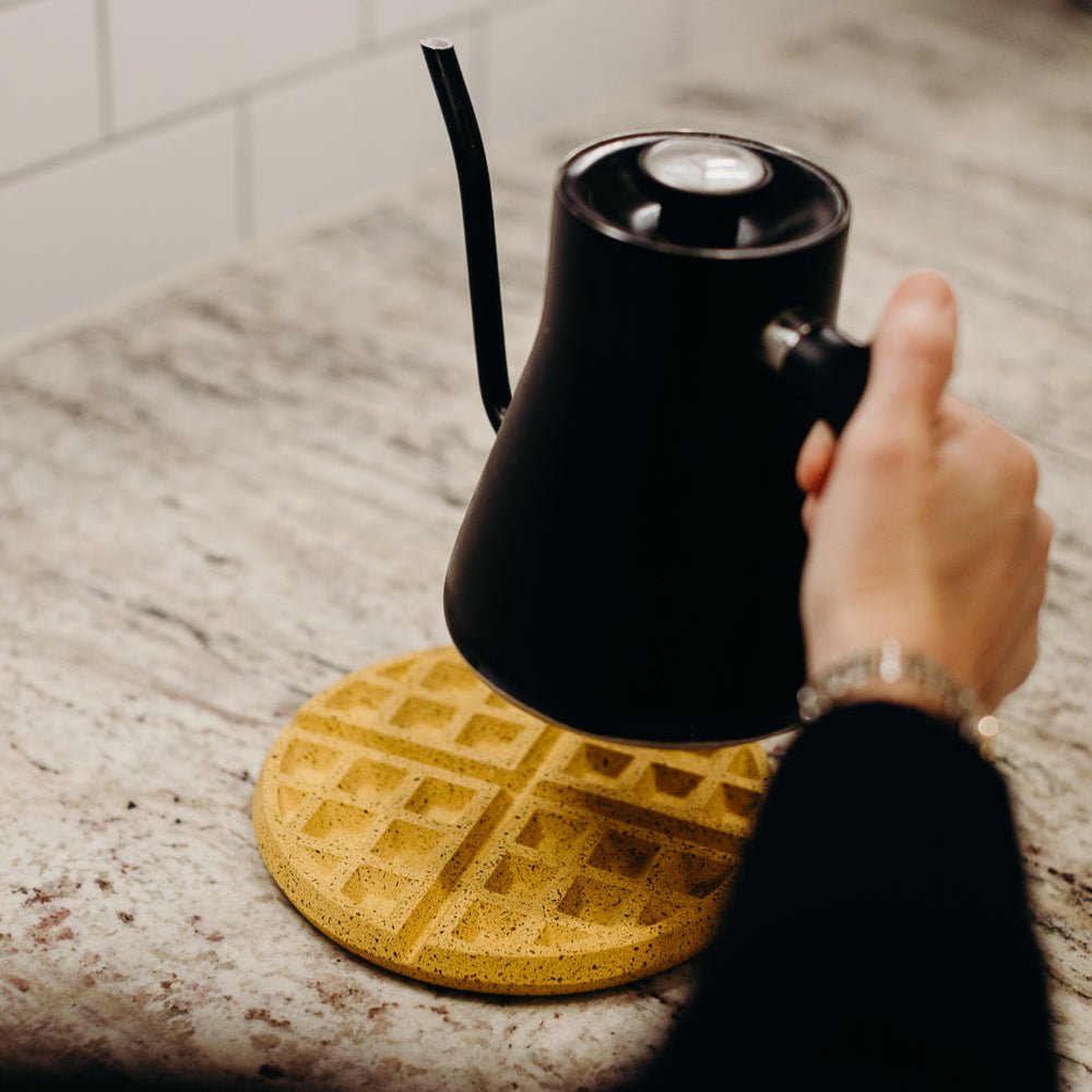 Black kettle on marigold terrazzo waffle trivet with diamond grid on light stone