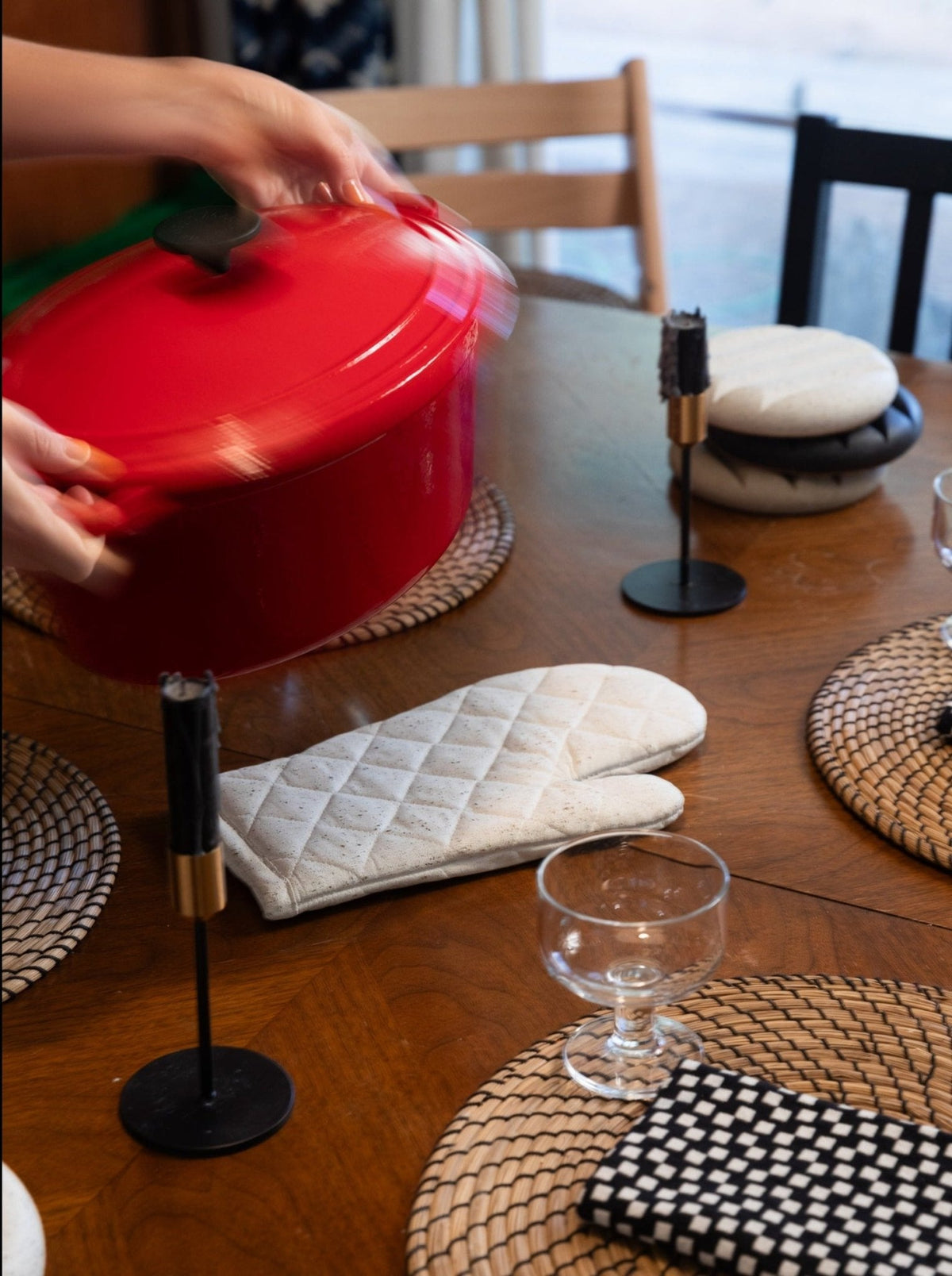 Hand lifting a red pot using a white terrazzo quilted oven mitt on the table.