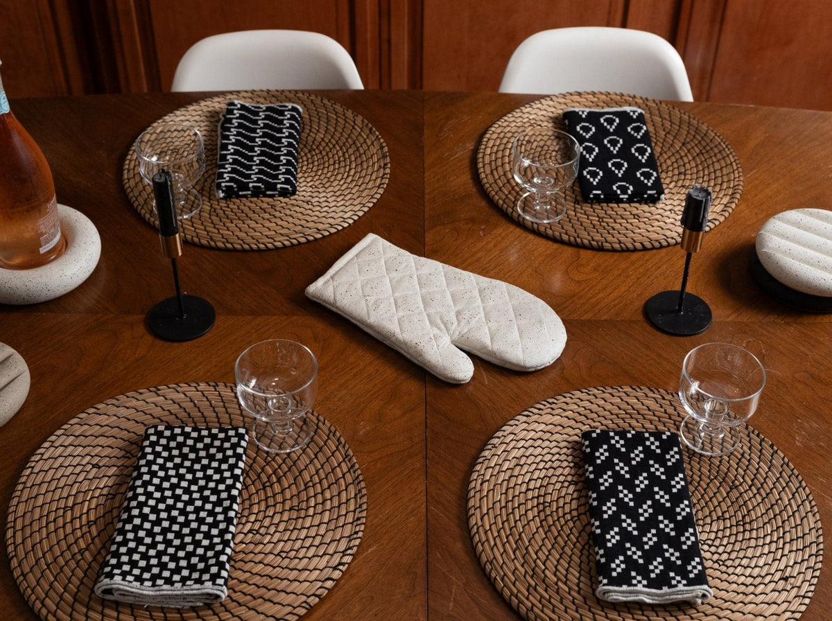 White quilted oven mitt with diamond stitching on a woven placemat at the table.