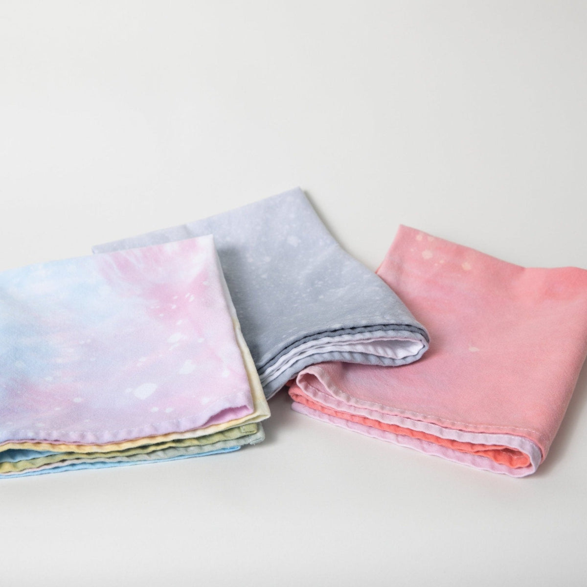 Folded hand-dyed tea towels close-up with pastel pink, blue, purple, gray, and yellow layers.
