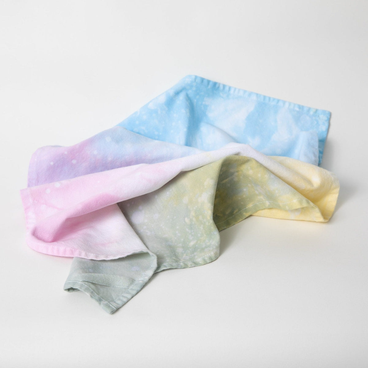 Stack of hand-dyed tea towels in pastel pink, blue, yellow, and sage with marbled dye.
