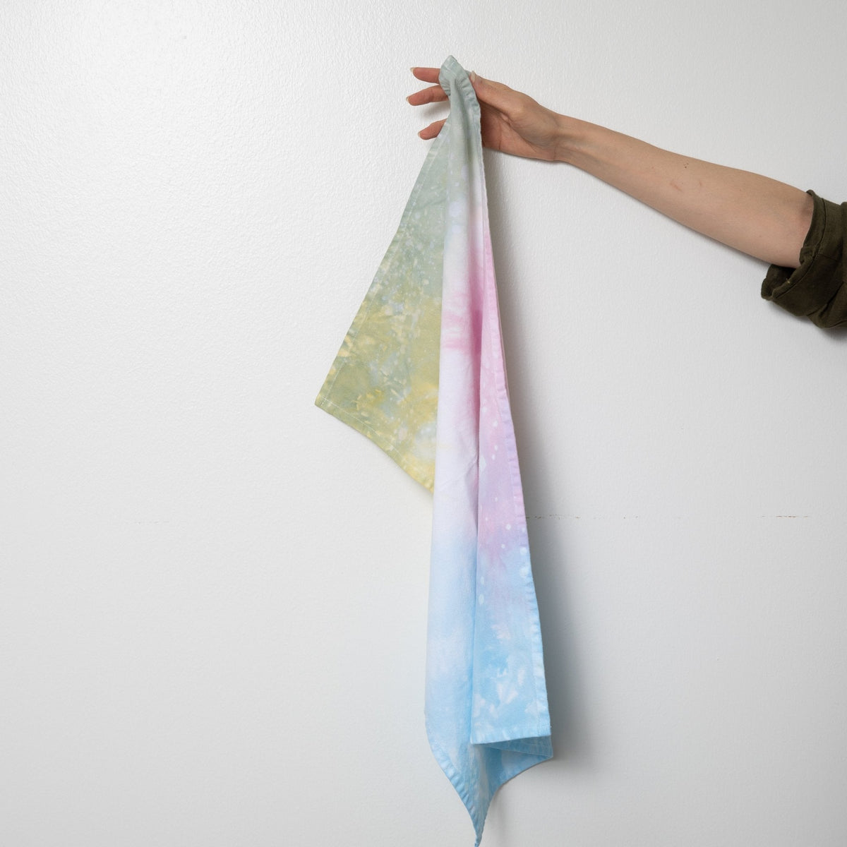 Hand-dyed tea towel in pastel green, pink, and blue with speckled pattern.