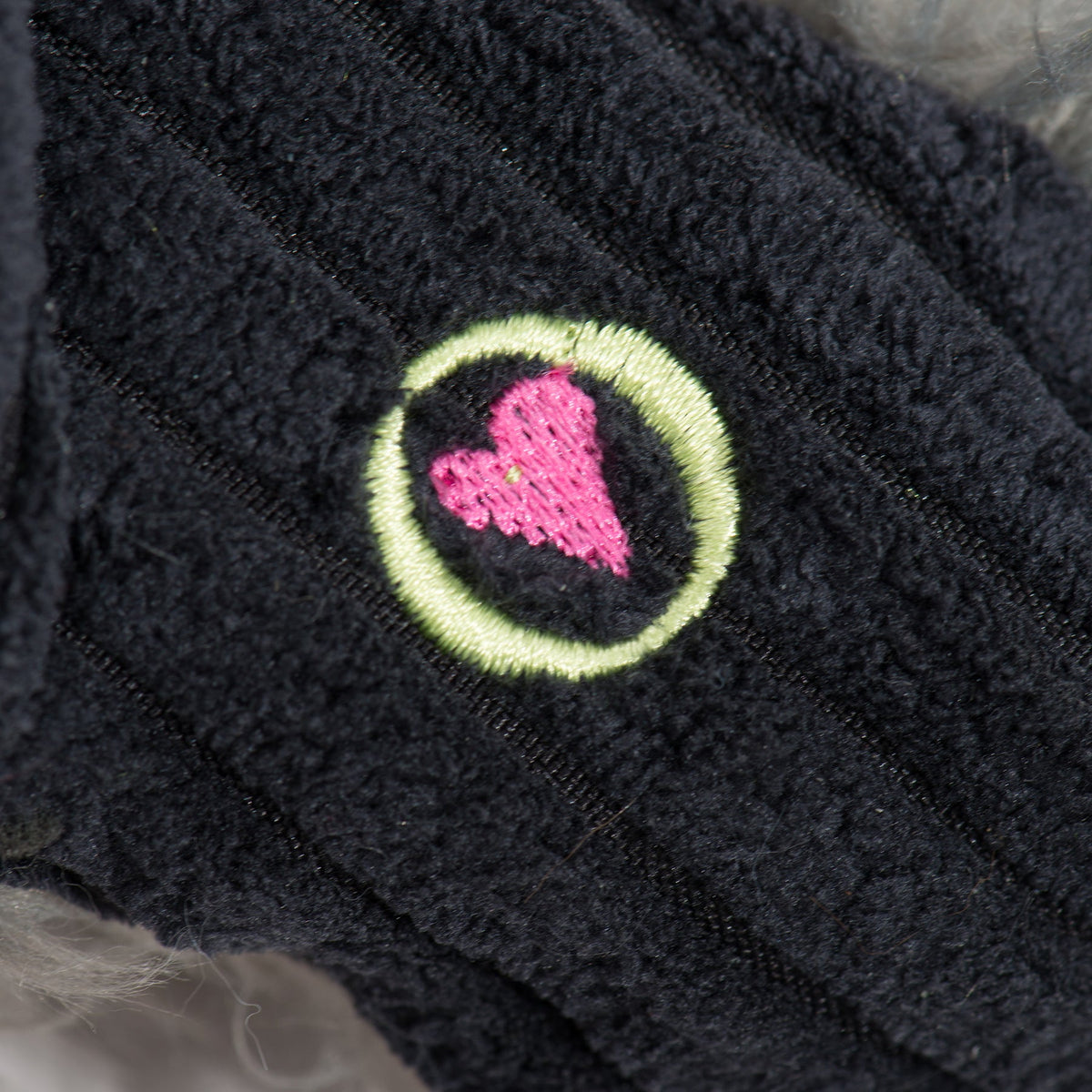 Close-up of pink heart emblem embroidered on the toy's black fabric