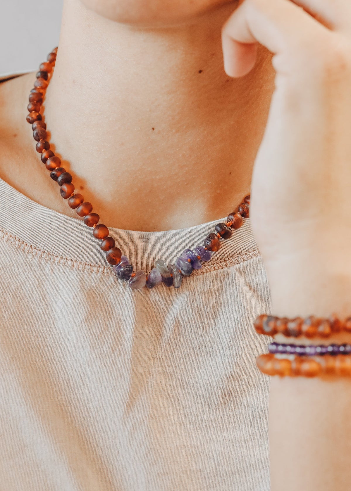 Amber beaded necklace with purple amethyst cluster, worn close-up at neckline.