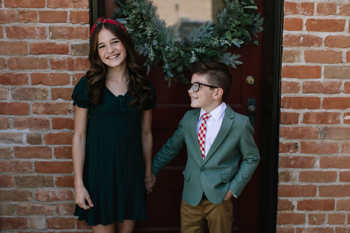 Red and white plaid necktie on a boys suit jacket, standing near brick wall