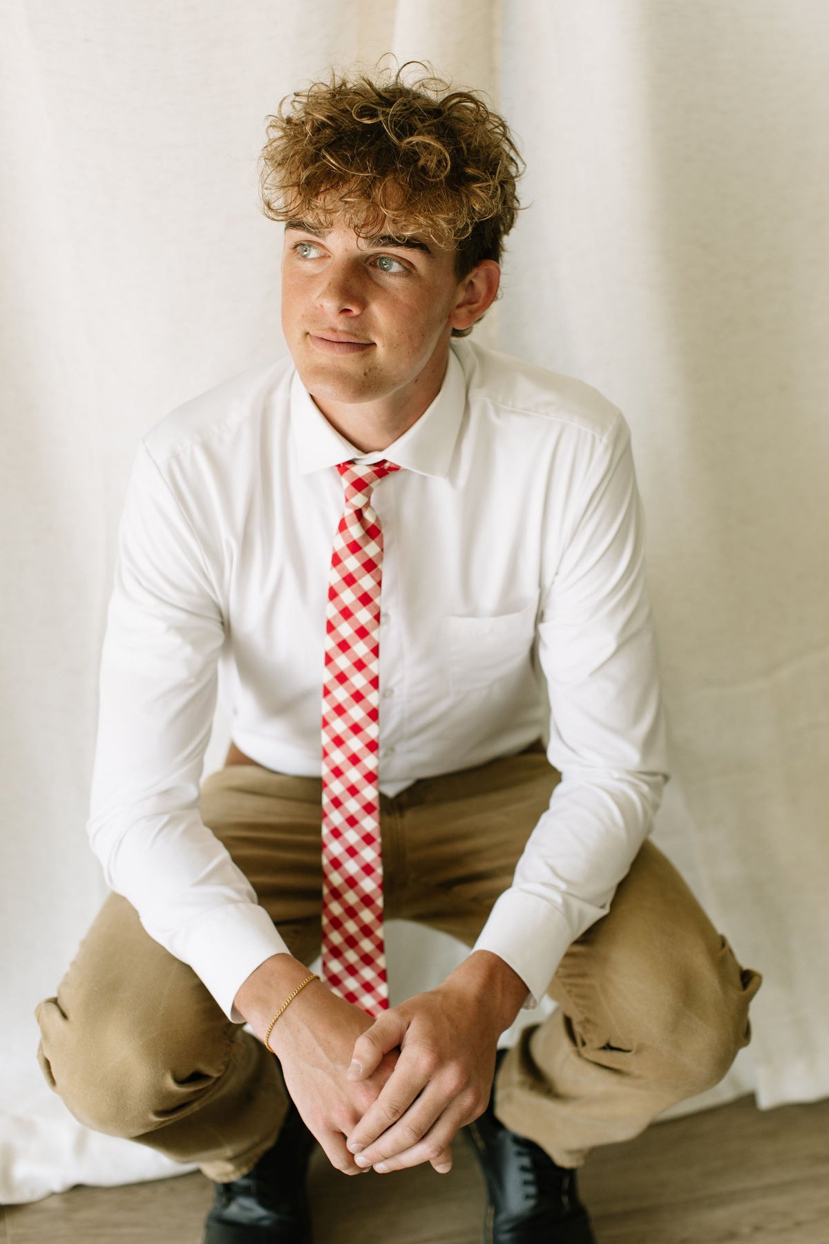 Men's red-and-cream plaid necktie worn on white shirt with khaki pants