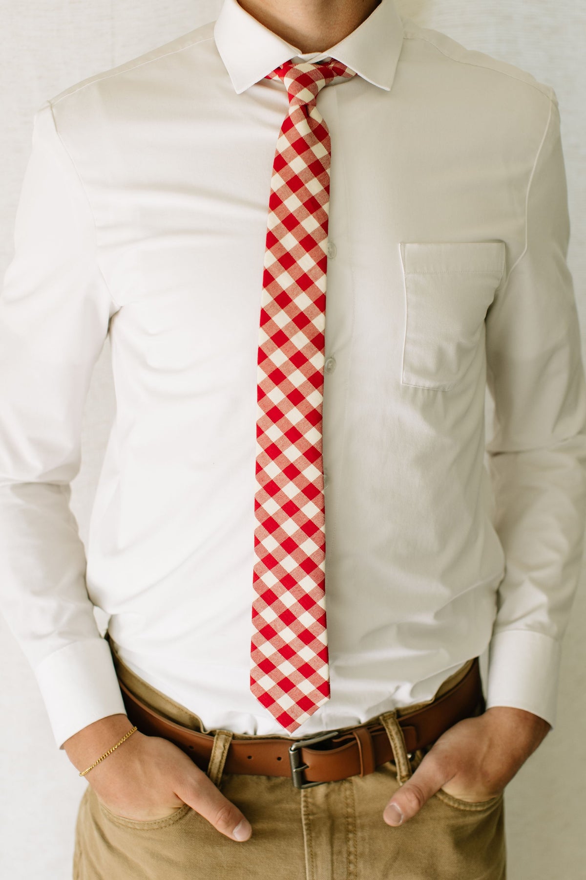 Men's red-and-cream plaid necktie on white shirt with hands resting at belt
