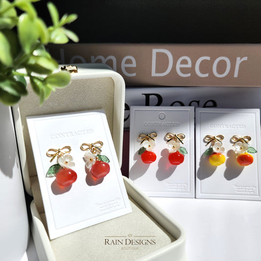 Gold apple-shaped dangle earrings: red fruit charms with white flowers and green leaves