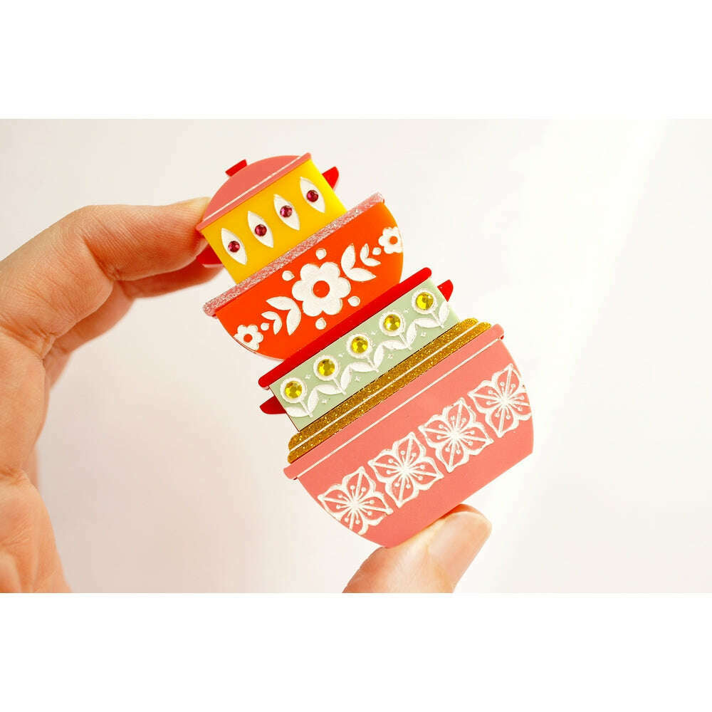 Stacked retro container brooch held in hand, red and white floral with green panels