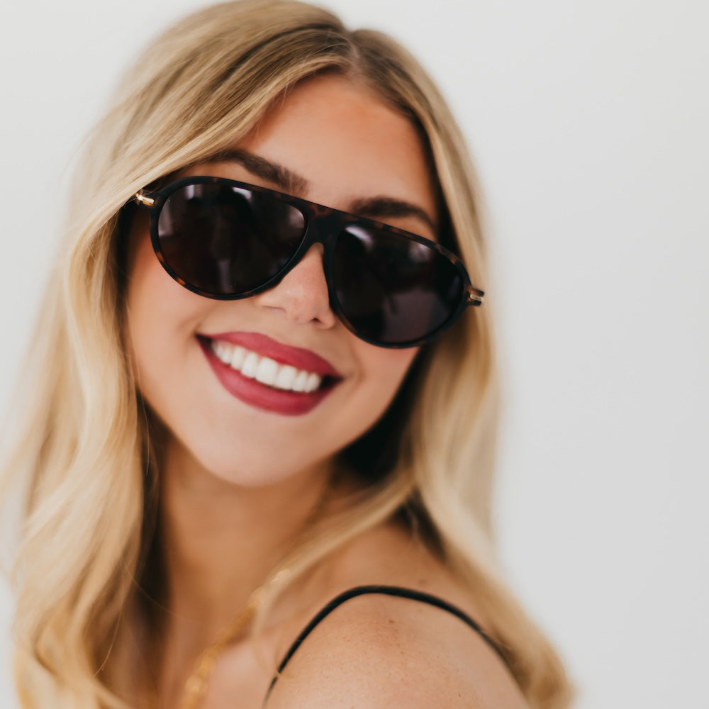 Oval sunglasses with black frame and dark lenses, gold-toned details