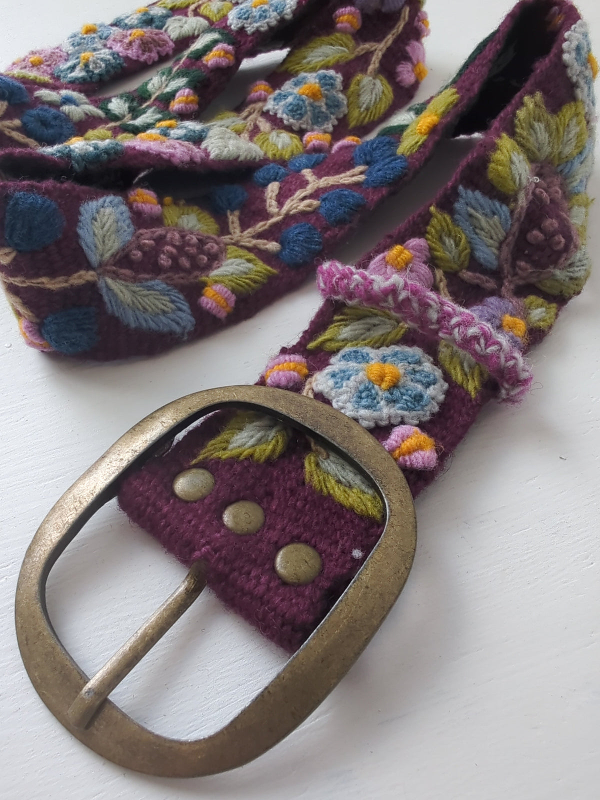 Plum embroidered wide belt close-up with brass oval buckle and floral stitching