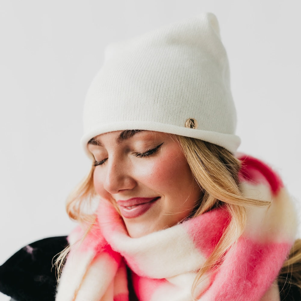 Close view of winter white beanie's rolled edge and small gold-tone logo