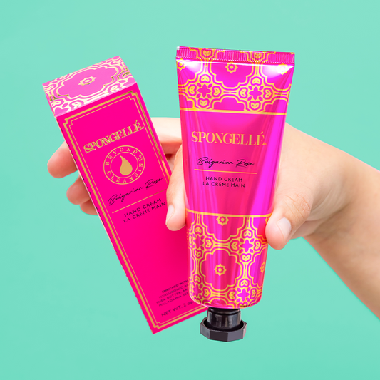 Hand holding pink SPONGELLE Bulgarian Rose hand cream tube with box beside it