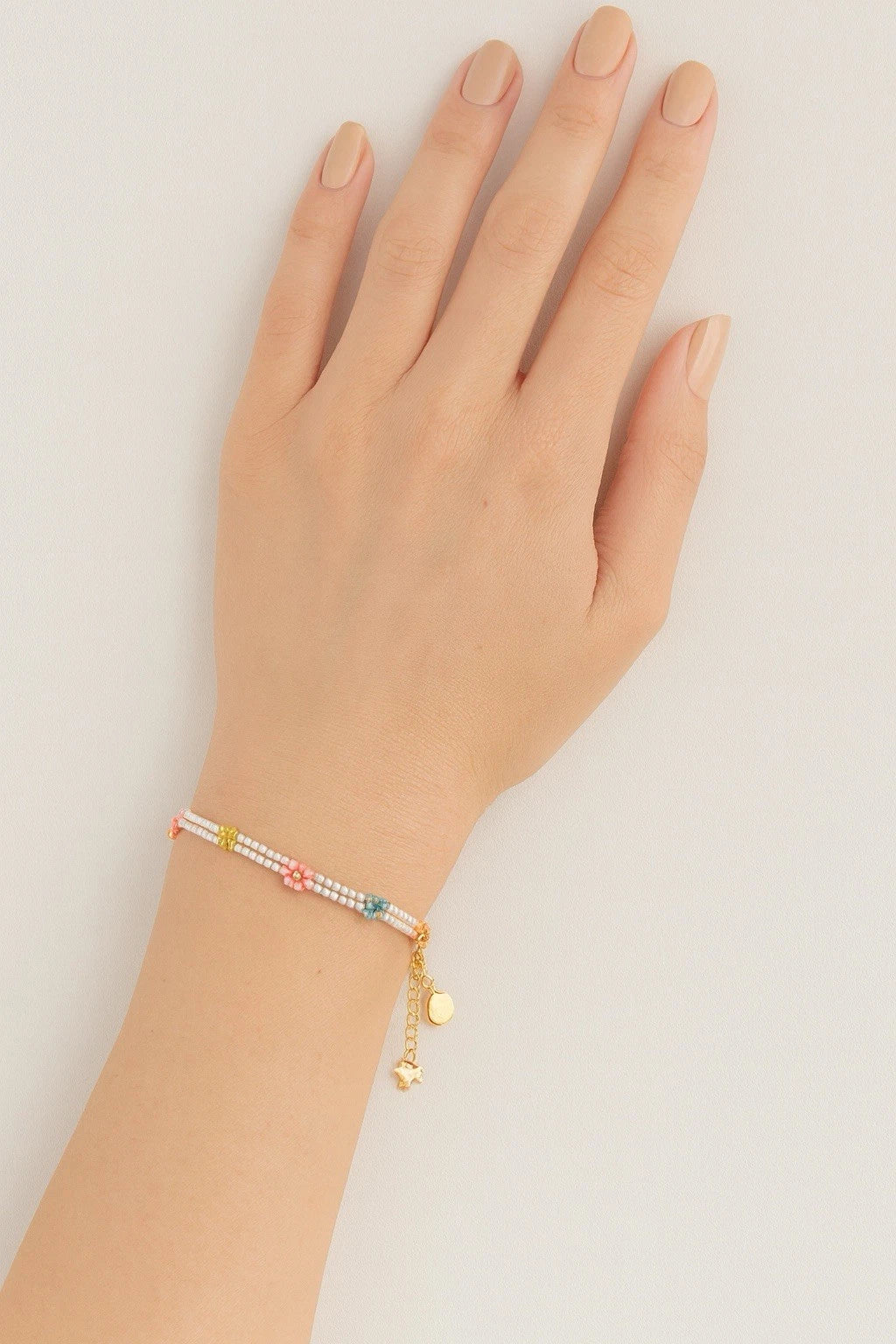 Multicolored beaded floral bracelet on wrist with gold chain and tiny bell charm