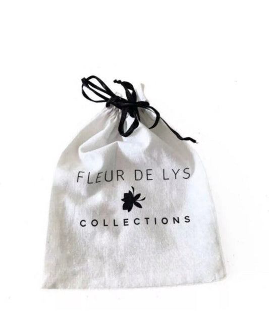 White drawstring pouch with black bow and text 'FLEUR DE LYS COLLECTIONS'