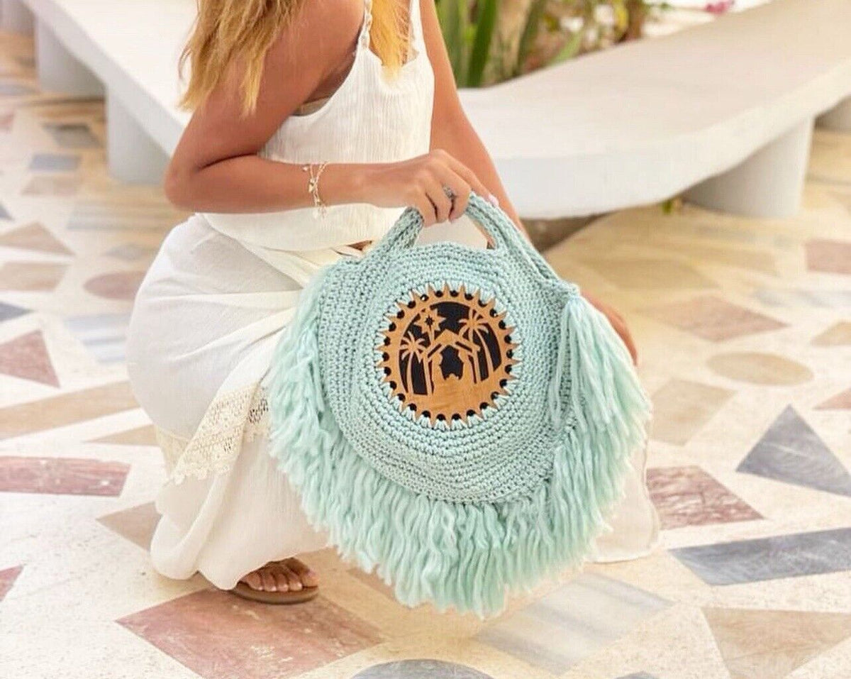 Turquoise fringe crochet bag with round carved wood emblem, carried on the lap
