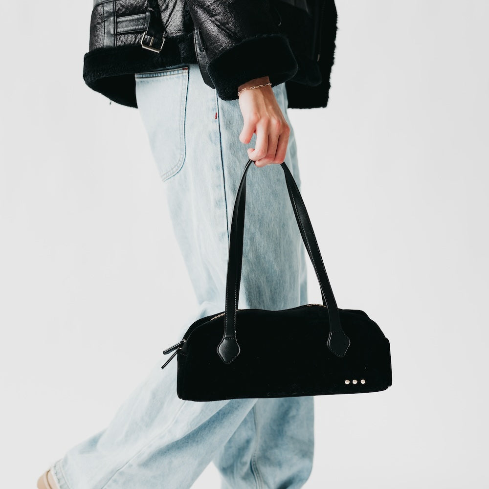 Black suede barrel shoulder bag with top zipper, long handles, metal stud detail