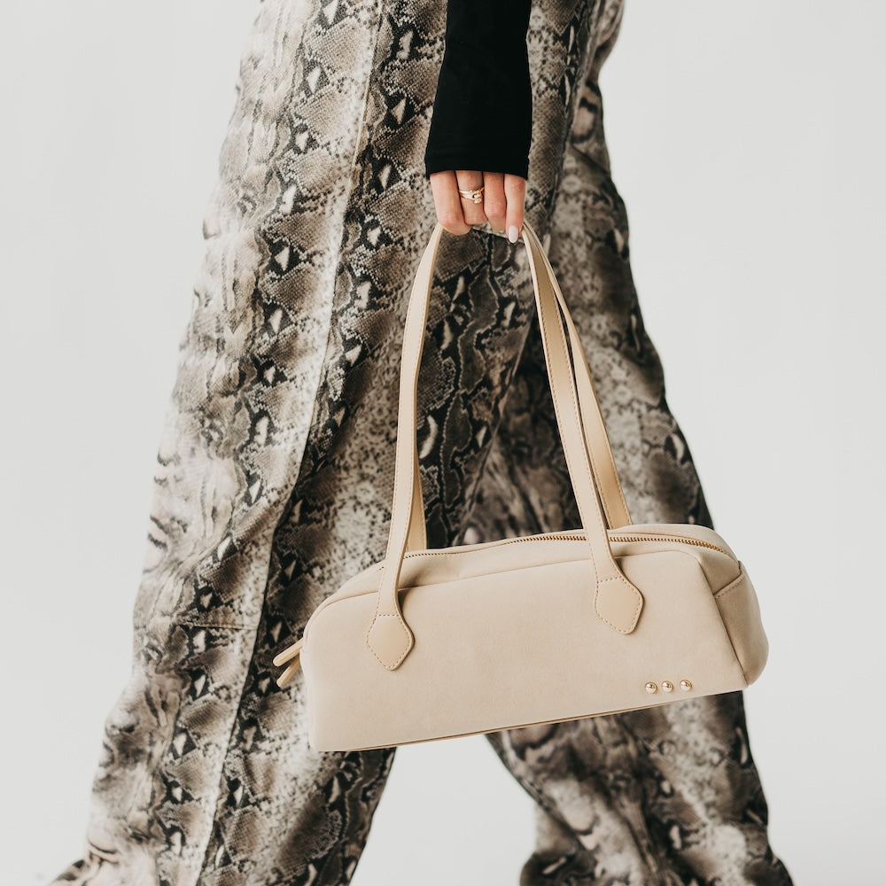 Beige suede barrel shoulder bag with top zipper, curved handles, metal studs
