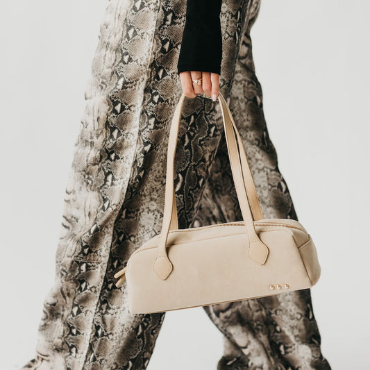 Beige suede barrel shoulder bag with top zipper, curved handles, metal studs