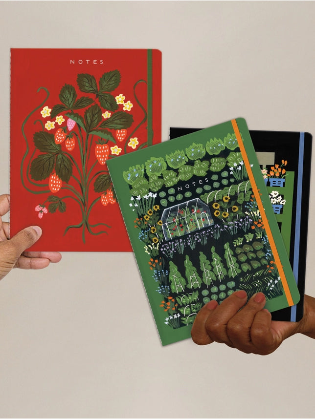 Set of three sewn notebooks with botanical covers, held in hands.