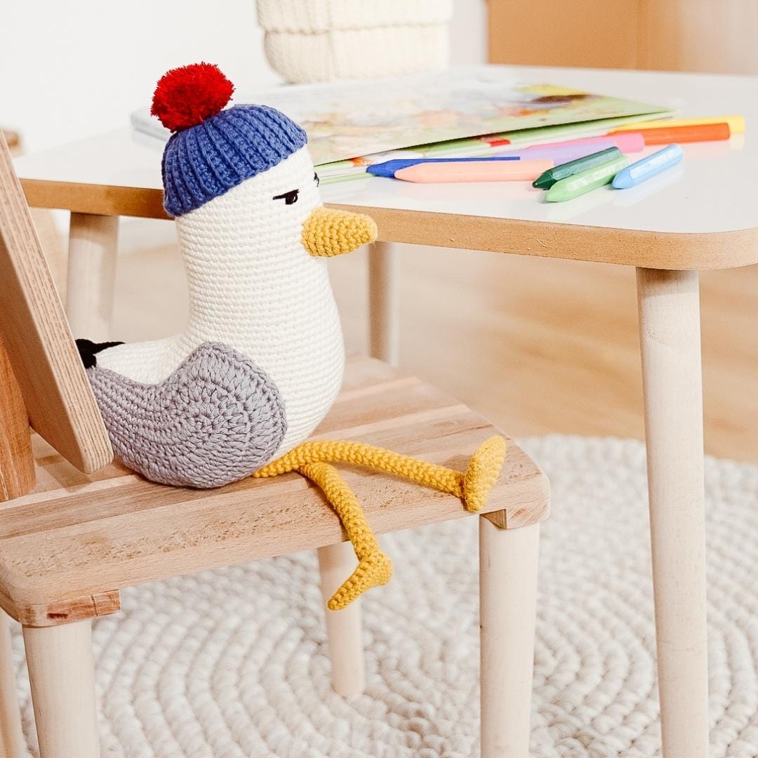 Crocheted seagull plush toy with a blue and red knit cap and long yellow legs