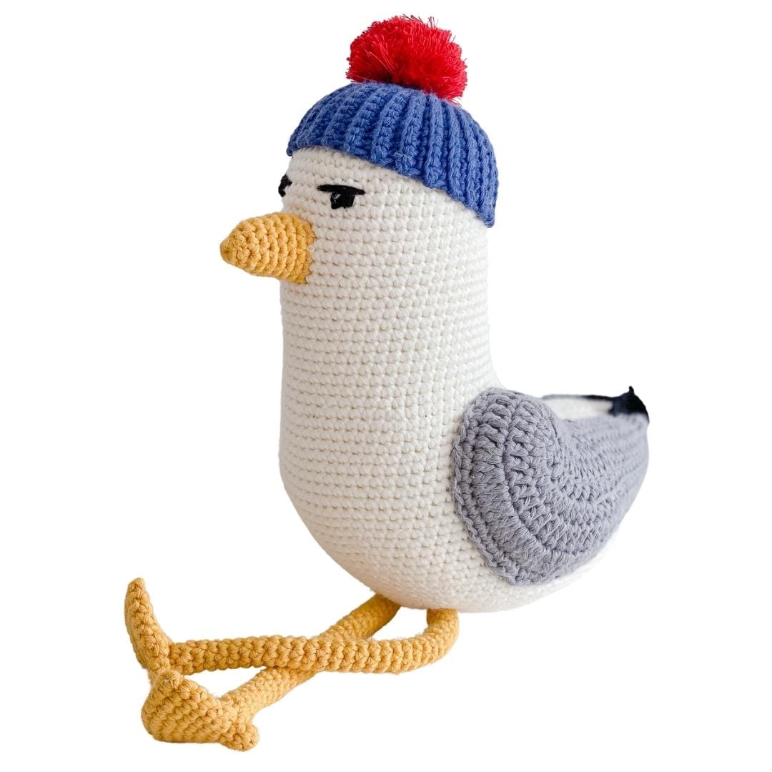 Crocheted seagull plush with a blue ribbed cap, red pom-pom, gray wings, and yellow feet