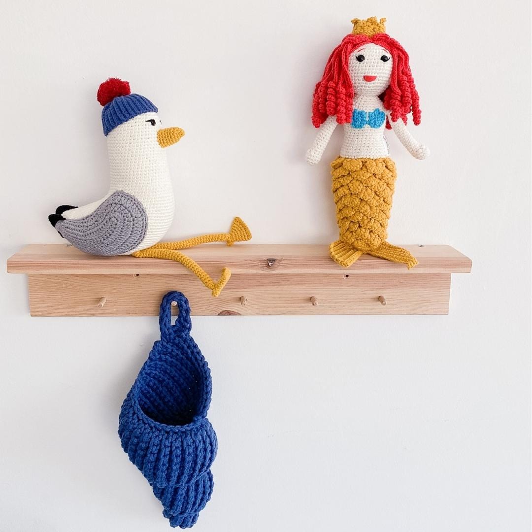 Crocheted seagull plush with a blue cap, red pom-pom, gray wings, and dangling yellow legs
