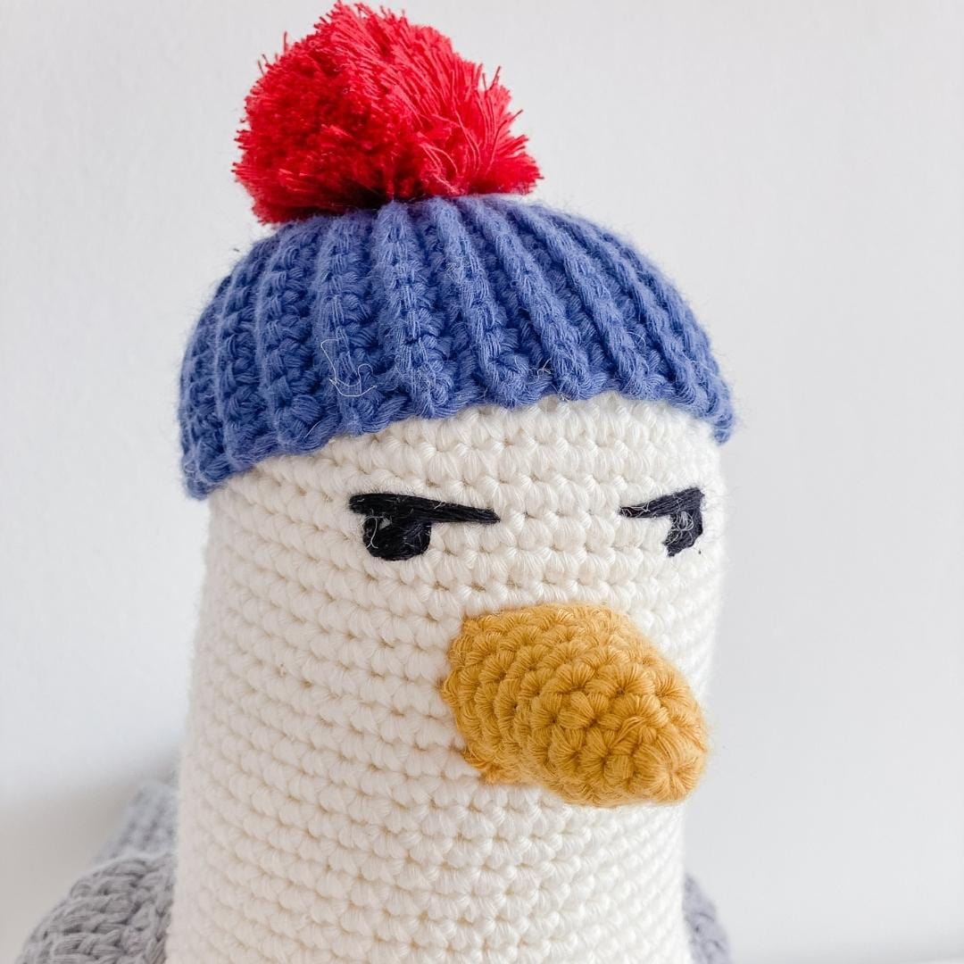 Close-up of the crocheted seagull's blue cap, red pom-pom, yellow beak, and stitched eyes