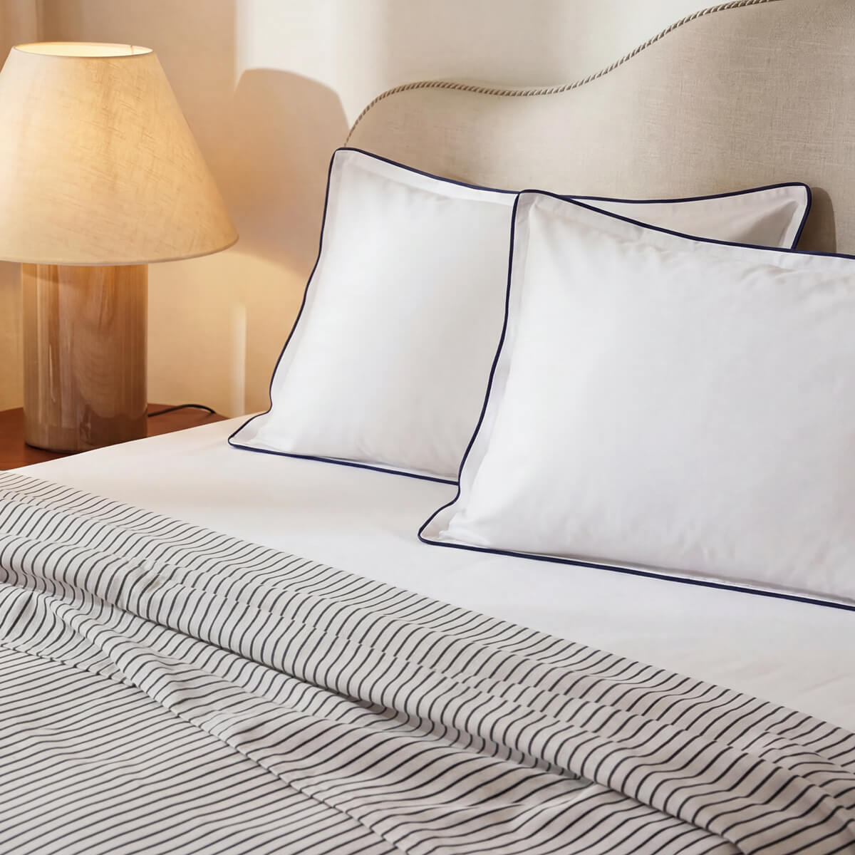 Striped cooling top sheet on bed with white pillows and dark piping trim