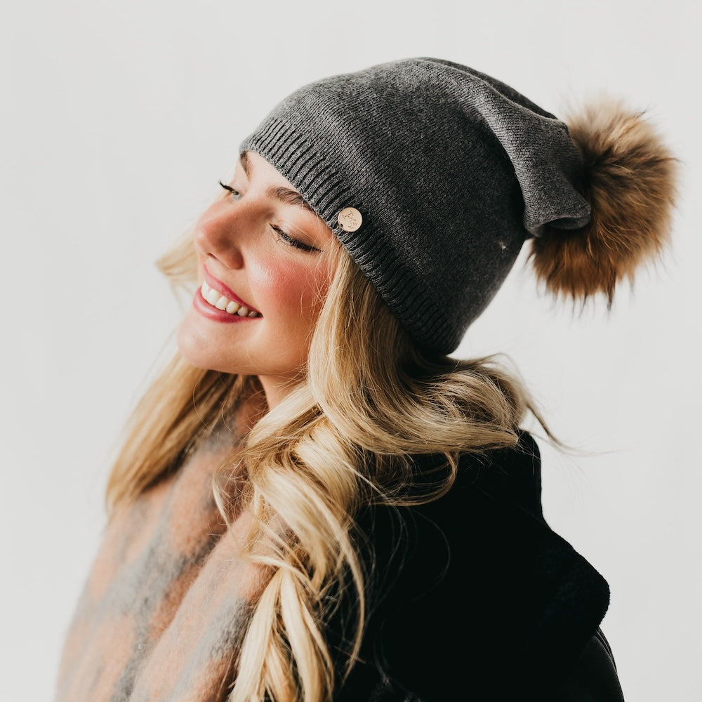 Dark gray knit beanie with slouchy crown, ribbed cuff, and fur pom