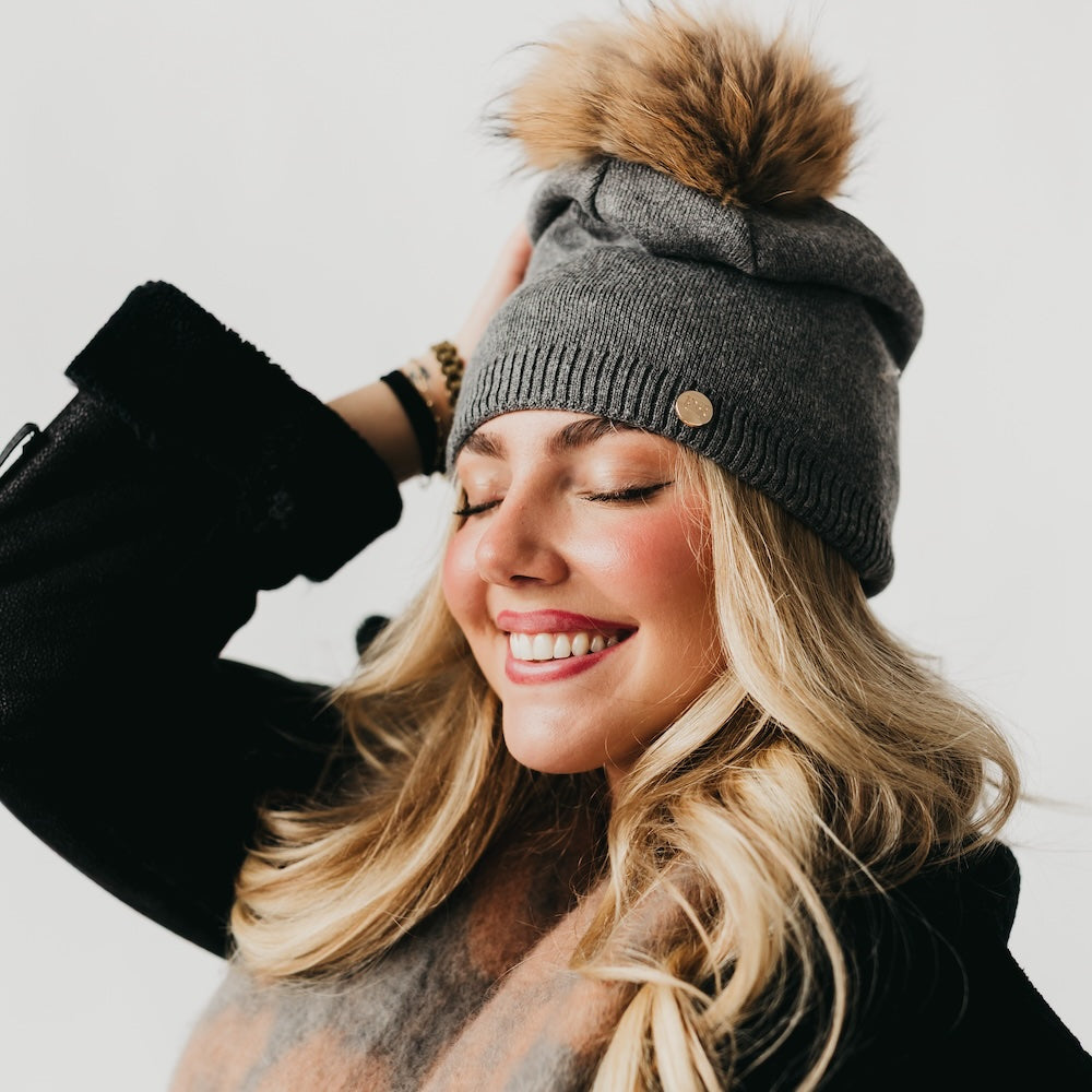 Charcoal knit slouchy beanie with ribbed cuff, gold-tone button, and tan fur pom