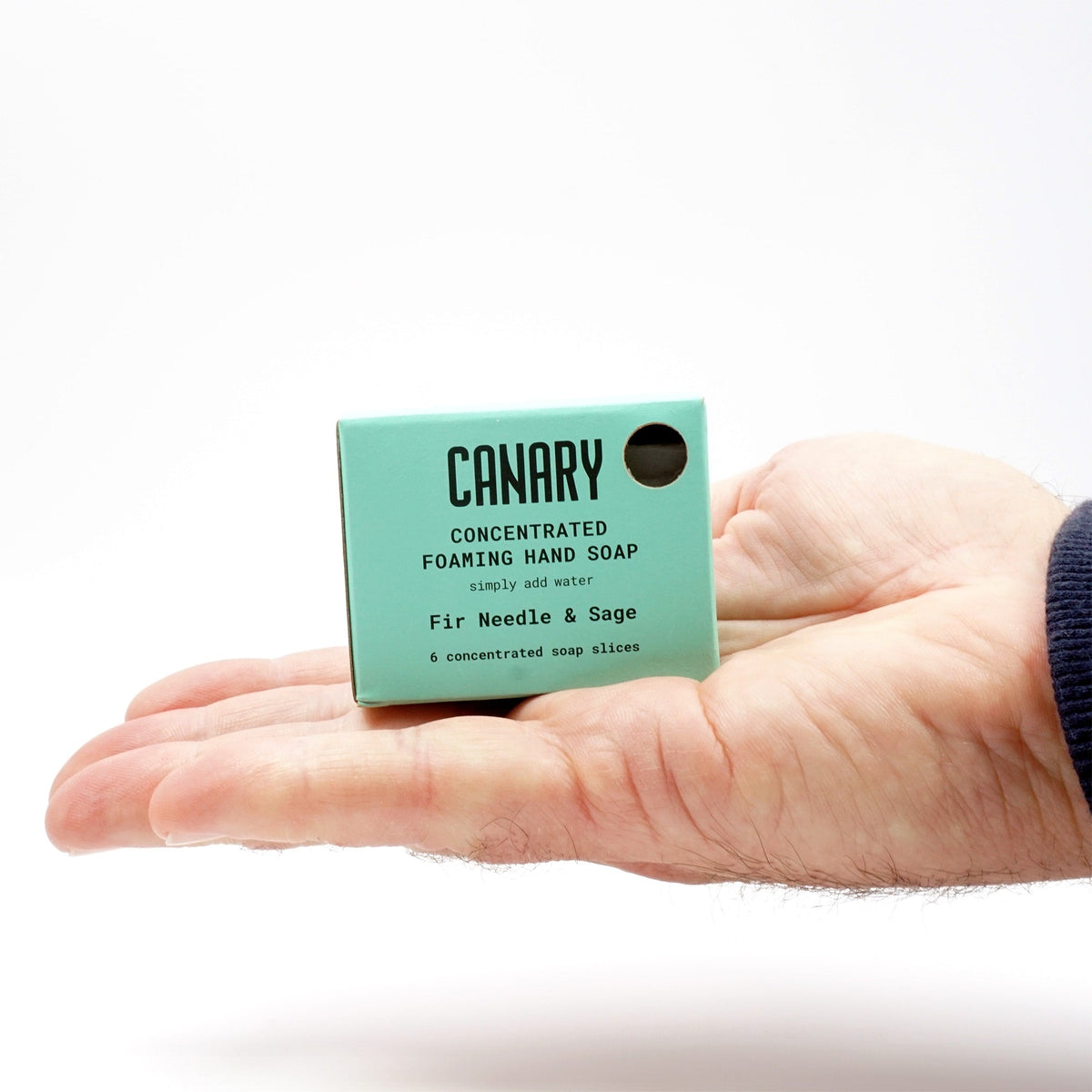 Fir needle and sage concentrated hand soap refill bars in a teal carton held in one hand.