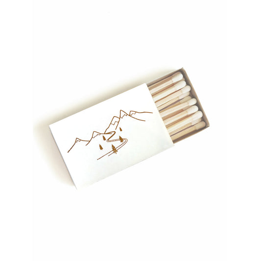 Gold-foil line-art matchbox with snowy mountain scene, open showing wooden matches