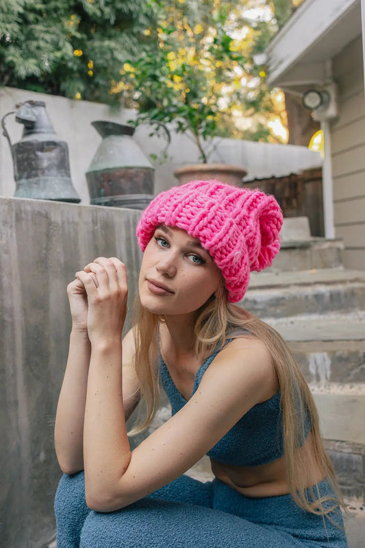 Hot pink cable-knit beanie with pom-pom top and ribbed cuff, worn on head