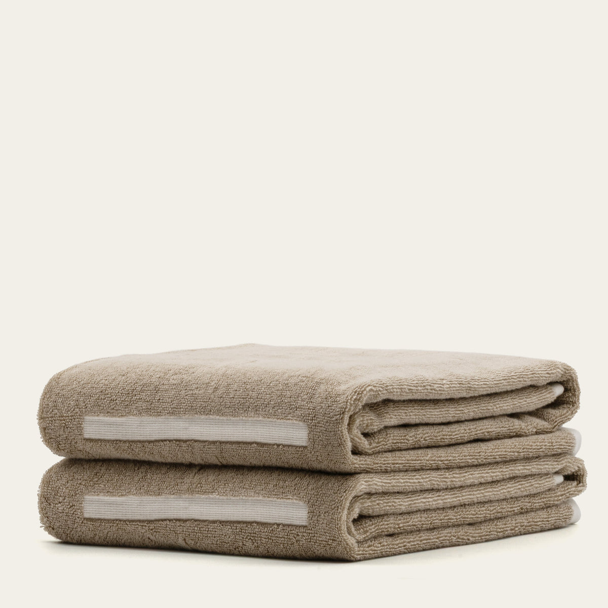 Two stacked tan cotton towels with ecru accent band, plush terry weave