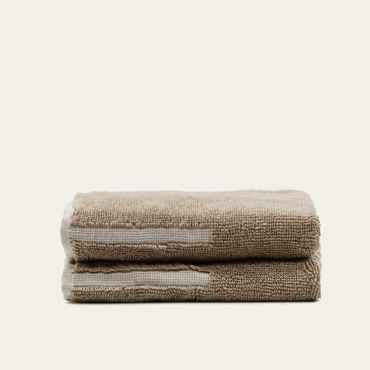 Rolled ecru cotton towel stack with subtle tan border stripe