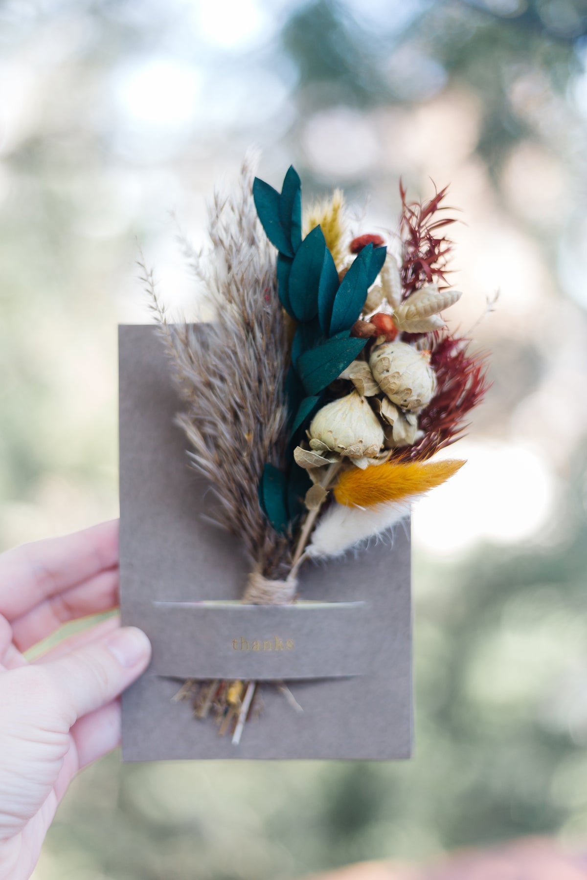 Dried mini bouquet greeting card held in hand, grey cover with teal leaves and white blooms