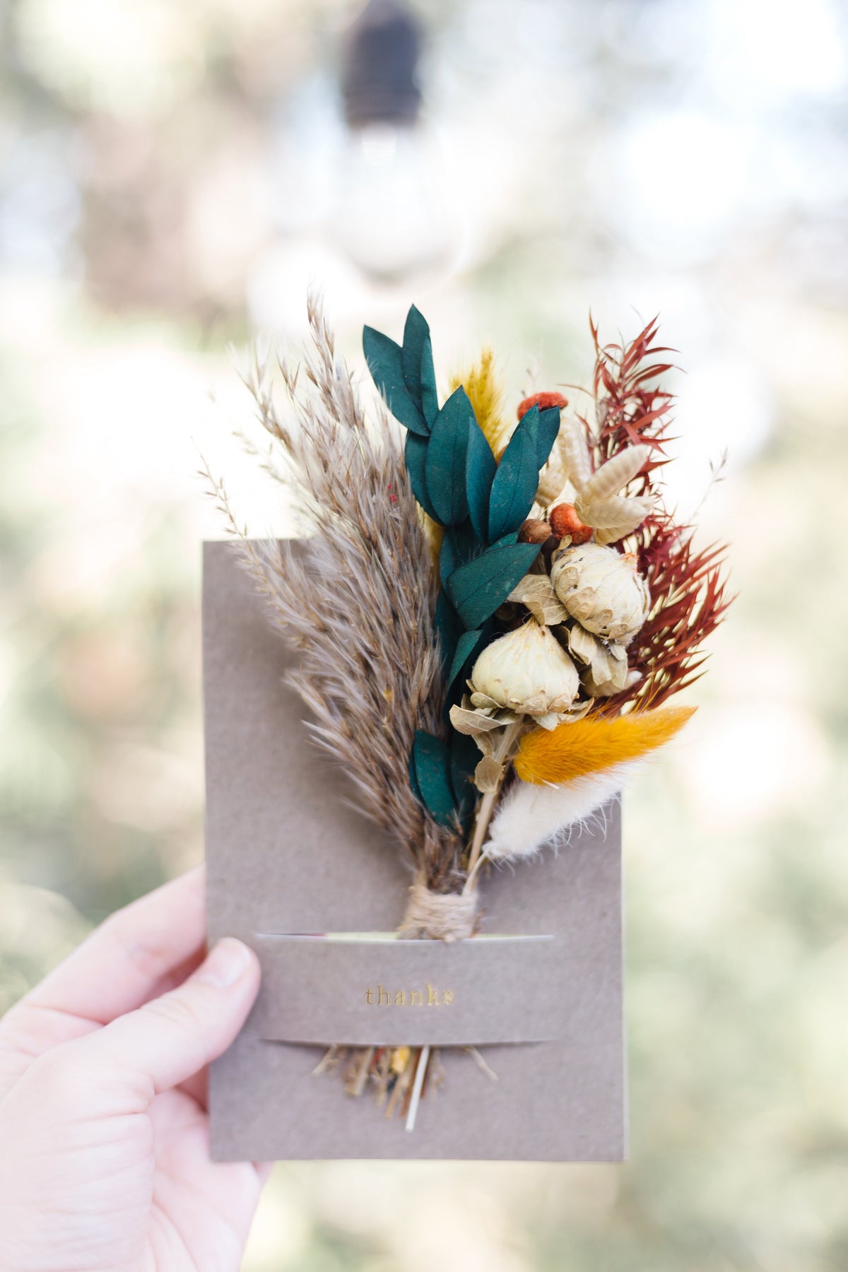 Kraft mini bouquet card held in hand with teal and beige dried flowers