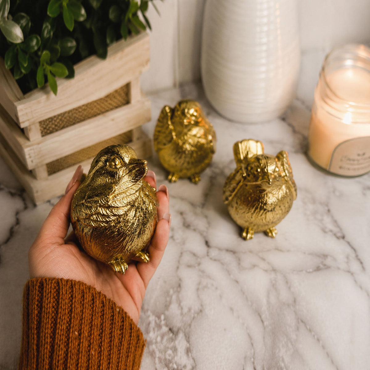 Gold-tone bird figurine held in hand beside two matching birds on a marble surface