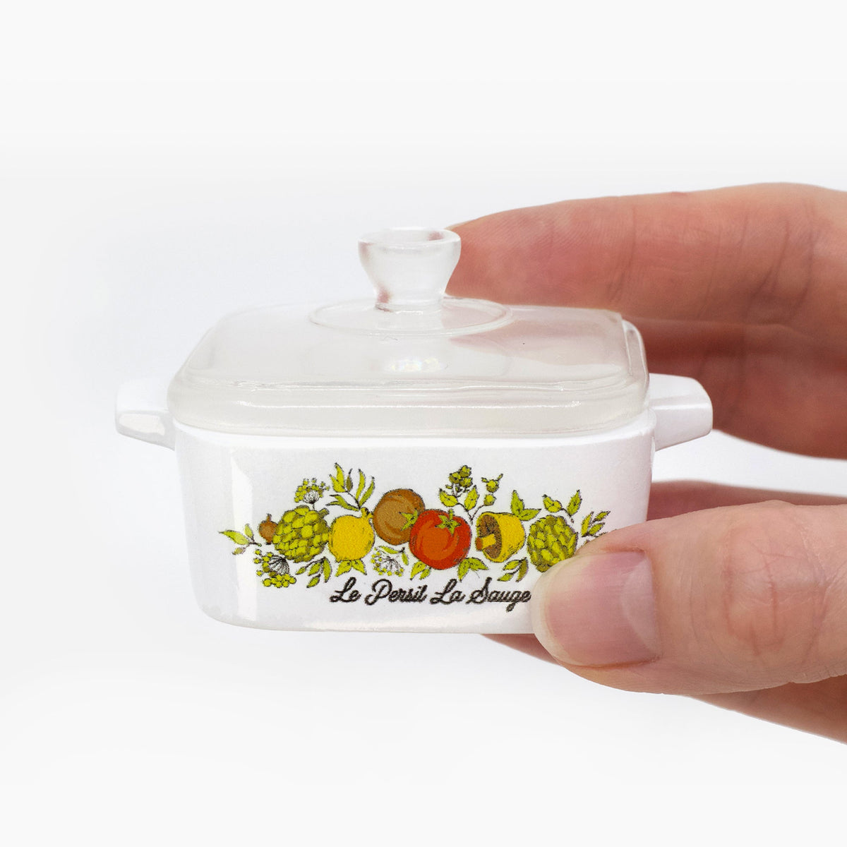 Mini trinket box with clear lid held open, white ceramic with fruit-and-herb graphic front