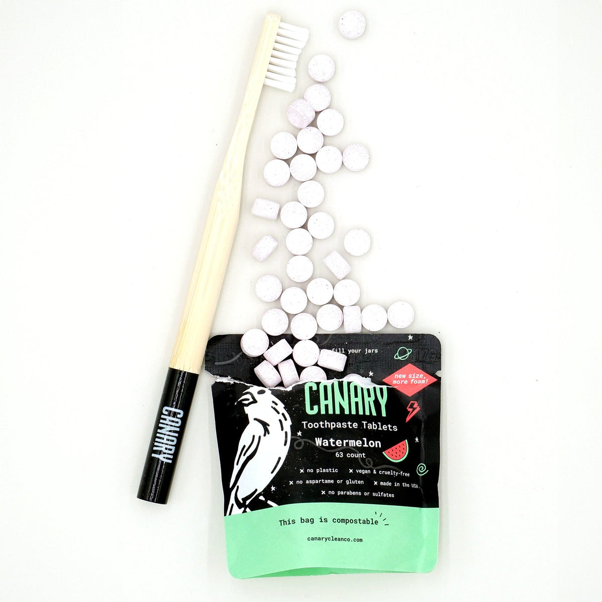 Watermelon toothpaste tablets spilled beside a compostable pouch and bamboo toothbrush.
