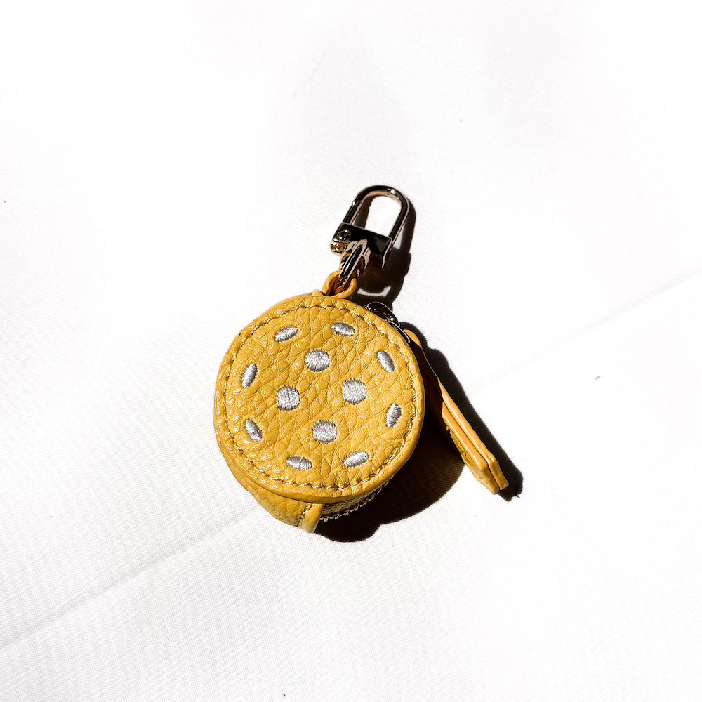 Yellow stitched sports bag charm ball with white dotted pattern on a gold keyring