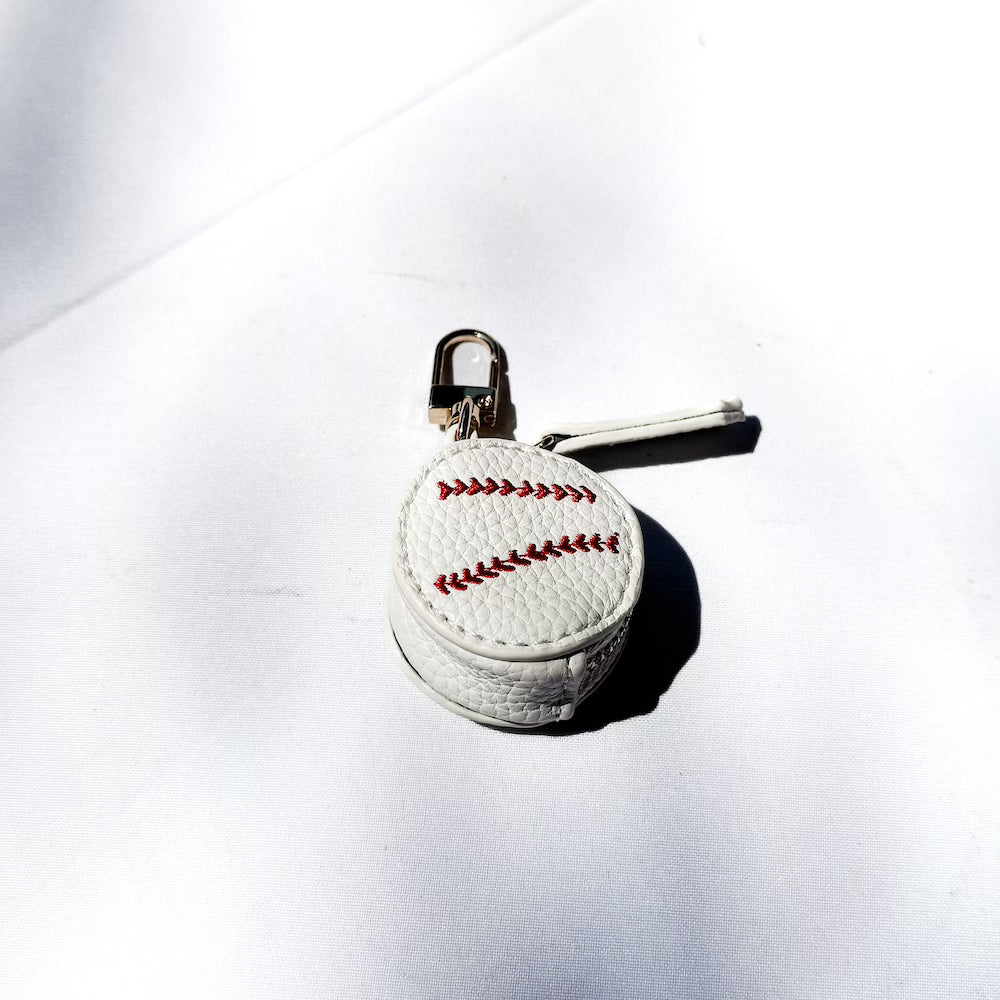White sports bag charm ball with red stitched seam on a gold keyring clip