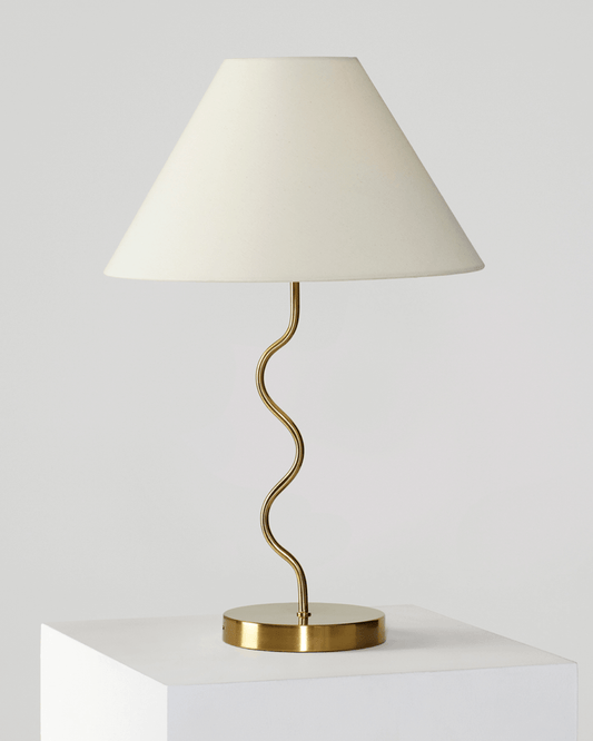 Brass table lamp with off-white fabric shade and wavy curved metal stem