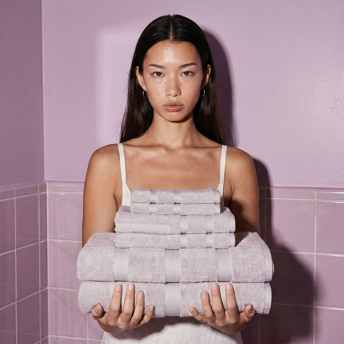 Stack of light gray cotton towels with stitched stripe bands, held against chest