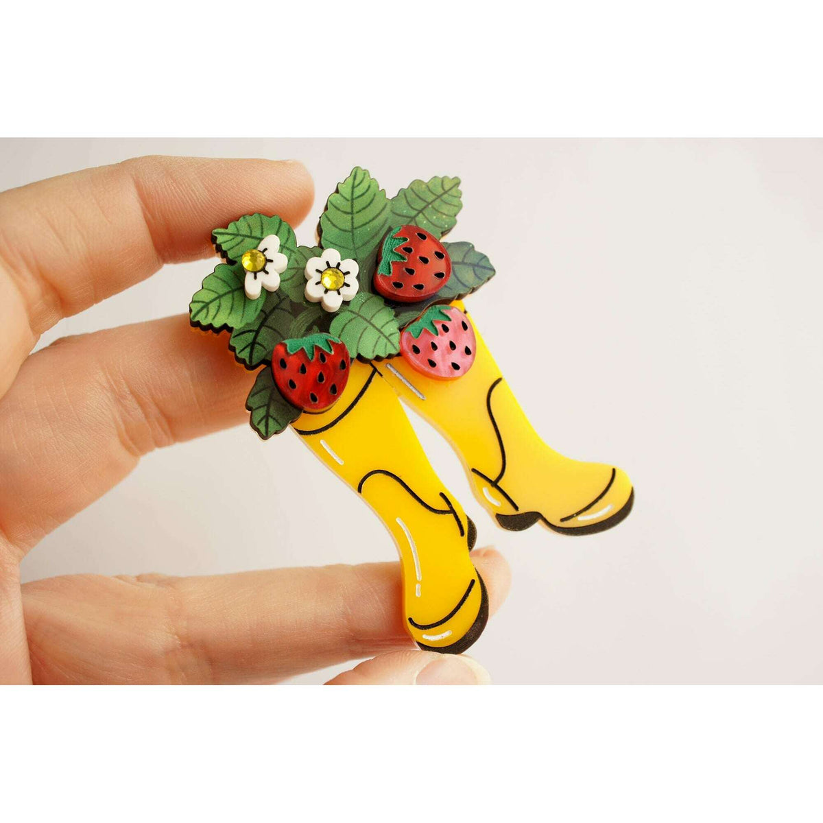 Yellow boot strawberry brooch shown in hand with red strawberries and small white flowers