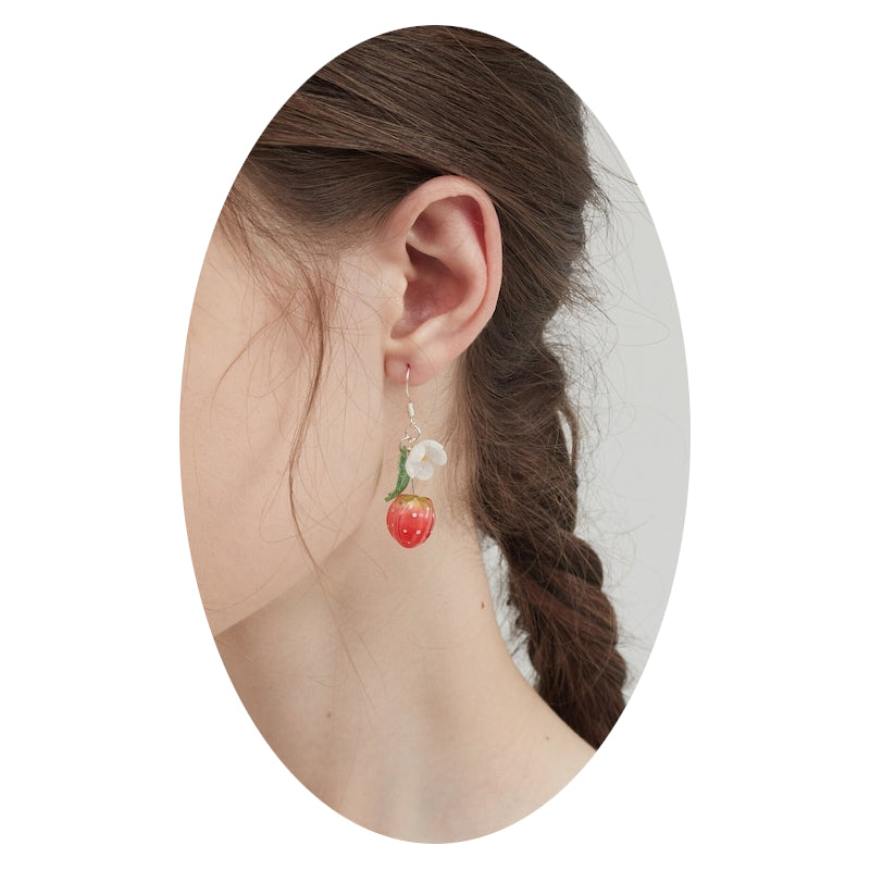 Strawberry and flower drop earrings on ear, with white blooms, green leaves, and red berries