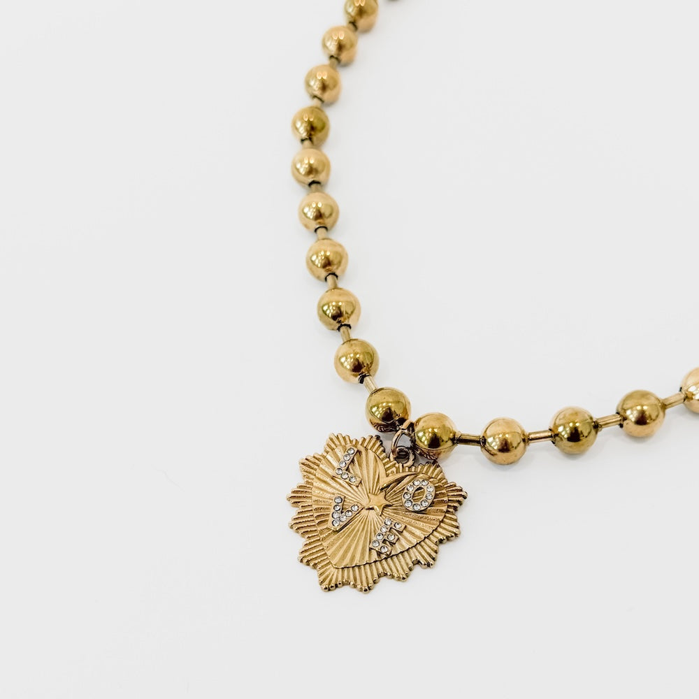 Close-up of gold-tone ball chain and sunburst heart pendant detail